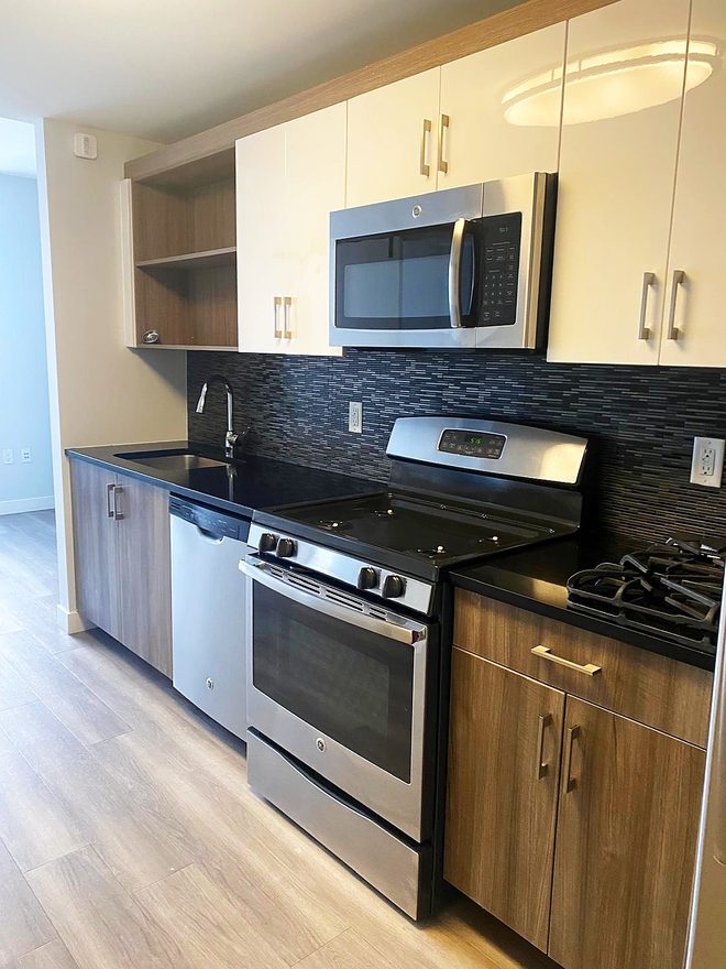 A finished kitchen with a clean range, microwave and dark tile backsplash
