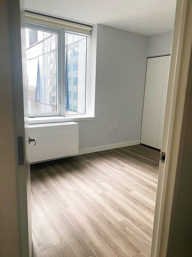 An empty bedroom with clean floor, closet doors and a window