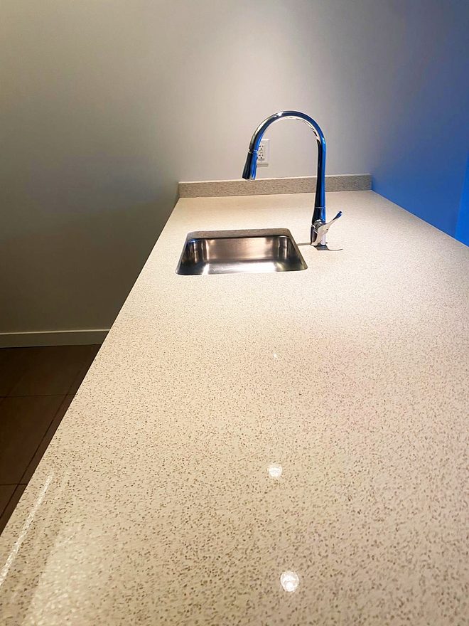 A clean stone counter with a small stainless bar sink and tap