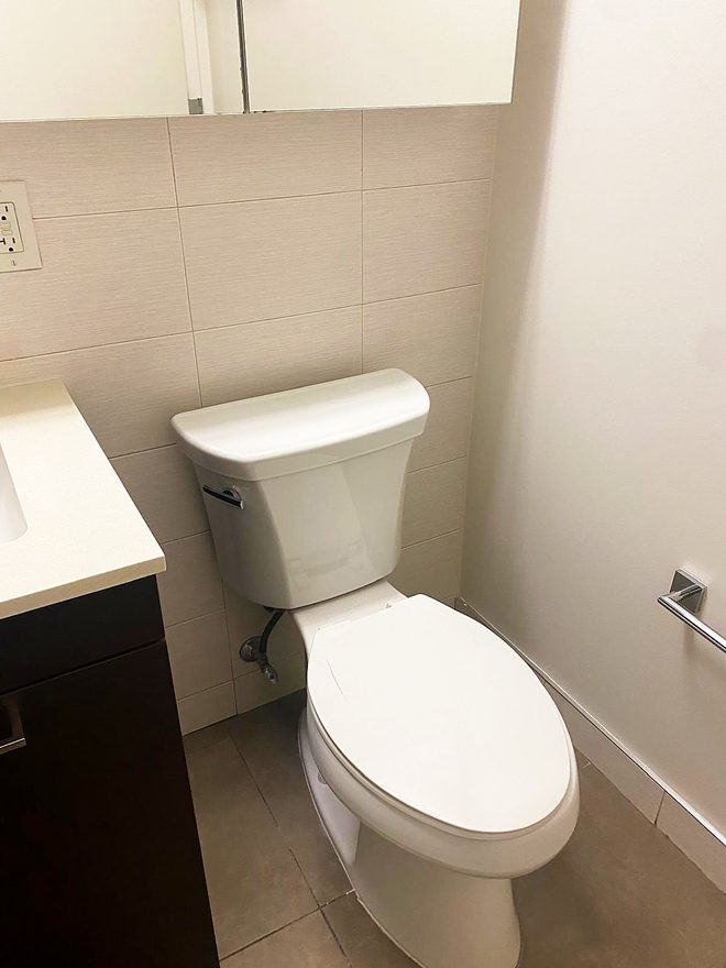 A clean toilet beside a vanity with tiled walls