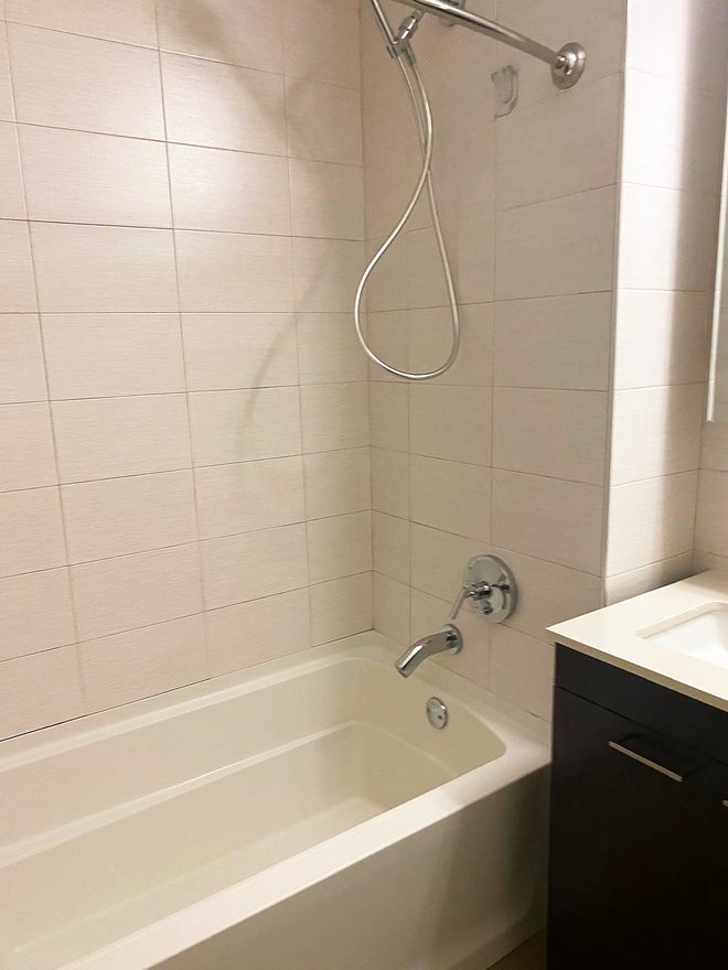 A clean tiled tub surround with shower head and taps